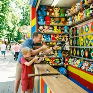 Отец с сыном стреляют в тире, стена с плюшевыми игрушками и мишенями